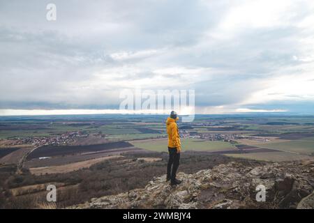 Voyageur en veste jaune se tient au sommet du mont Rip et pointe vers la ville de Prague. Explorer le pays tchèque. Banque D'Images