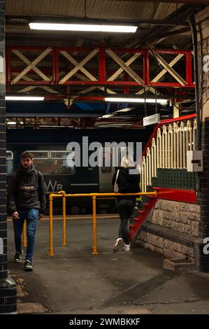 La sortie au quai 1 de la gare de Teignmouth avec une femme blonde attendant et un homme sortant alors que le train est à l'arrêt avec des passagers. Banque D'Images