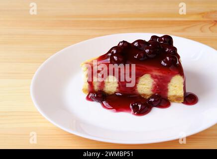 Assiette d'une tranche de délicieux cheesecake cuit au four avec sauce aux myrtilles sur une table en bois Banque D'Images