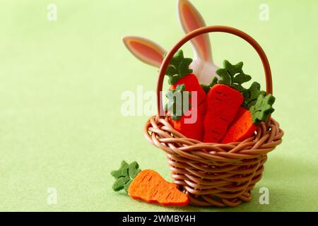 Panier avec des carottes mignonnes et des oreilles de lapin sur fond vert, concept de décoration de pâques Banque D'Images