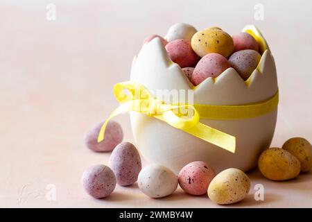 Chocolat coloré oeufs de pâques bonbons dans un bol en forme de coquille d'œuf sur fond rose, bonbons de pâques, décoration Banque D'Images