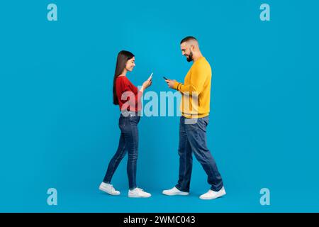 Communication et technologie. Couple souriant utilisant des smartphones tout en marchant devant l'autre Banque D'Images