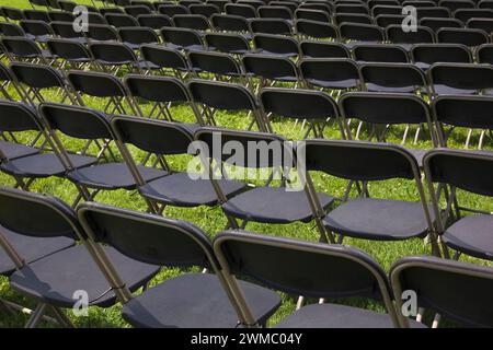 Rangées de fauteuils pliants en aluminium brun et en plastique noir sur herbe verte aménagées pour les spectateurs assistant à un événement en été. Banque D'Images