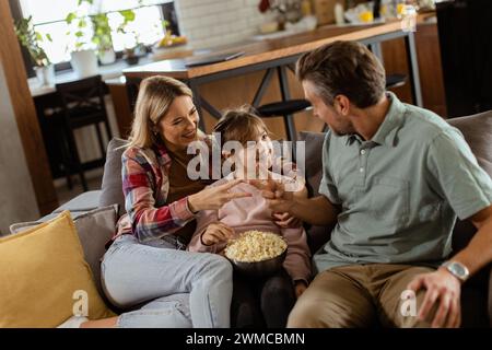 Un joyeux salon familial sur le canapé, s'engageant dans une conversation ludique avec un bol de pop-corn Banque D'Images