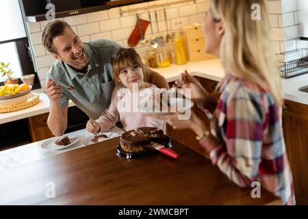 Une scène réconfortante se déroule alors qu'une famille savoure un appétissant gâteau au chocolat ensemble dans la chaleur de leur cuisine ensoleillée, partageant sourires et crèmes Banque D'Images