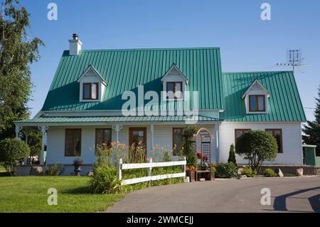 Maison à deux étages de style canadien ancien avec toit en tôle verte et cour avant paysagée en été. Banque D'Images