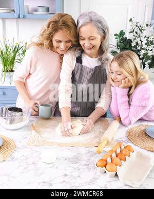 Grand-mère, maman et petite-fille se lient sur la cuisson, mélangeant la pâte sur la table de la cuisine en utilisant de la farine, des œufs et du lait Banque D'Images