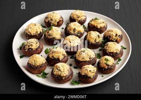 Champignons faits maison farcis au parmesan à l'ail sur une assiette sur un fond noir, vue de côté. Banque D'Images