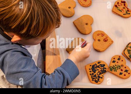 Jeune enfant de 5 ans décorant des biscuits en forme de coeur en pain d'épices pour Noël Banque D'Images
