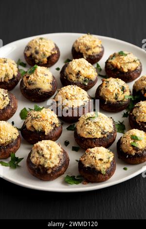 Champignons faits maison farcis au parmesan à l'ail sur une assiette sur un fond noir, vue de côté. Banque D'Images