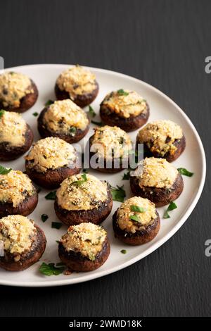 Champignons faits maison farcis au parmesan à l'ail sur une assiette sur un fond noir, vue de côté. Banque D'Images