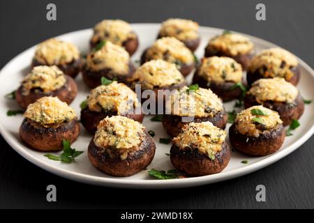 Champignons faits maison farcis au parmesan à l'ail sur une assiette sur un fond noir, vue de côté. Banque D'Images