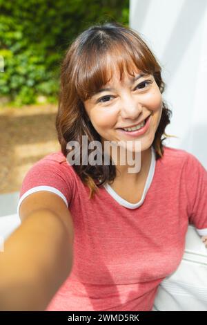 Une jeune femme biraciale joyeuse prend un selfie à l'extérieur Banque D'Images