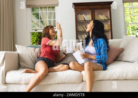 Deux jeunes femmes biraciales partagent un moment joyeux sur un canapé à la maison Banque D'Images