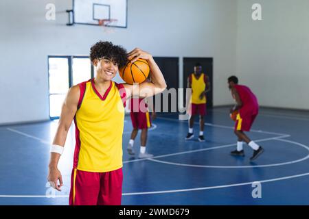 Un jeune homme biracial tient un basket-ball dans un court intérieur Banque D'Images