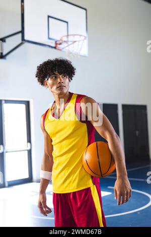 Un jeune homme biracial tient un basket-ball dans une salle de gym Banque D'Images