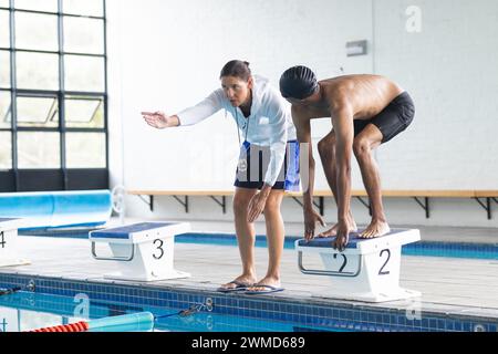 Caucasien entraîneur de femme instruit jeune athlète masculin biracial nageur près de la piscine avec espace de copie Banque D'Images