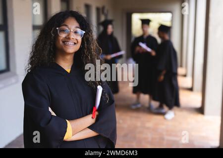 Fier diplômé en casquette et robe détenant un diplôme à l'école secondaire Banque D'Images