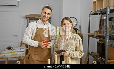 Un homme et une femme charpentiers avec café et tablette sourire dans un atelier. Banque D'Images