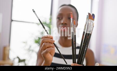 Dans son studio d'art, la femme artiste afro-américaine, engrossée et détendue, prend une décision cruciale, choisissant le pinceau parfait pour respirer la vie Banque D'Images