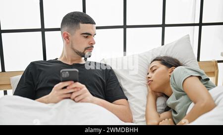 Scène enchanteresse de beau couple confortablement relaxant dans le lit, homme texto sur smartphone alors que sa petite amie dort dans leur chambre joliment décorée Banque D'Images