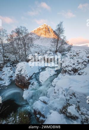 Cascade d'hiver au pied d'une montagne enneigée avec un pic ensoleillé le matin. Cascade Etive Mor. Buachaille Etive Mor. Scottish Highlands, Écosse Banque D'Images