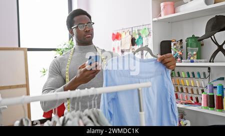 Homme afro-américain examinant une chemise dans un magasin de tailleur avec des fils à coudre colorés en arrière-plan. Banque D'Images