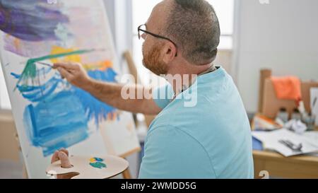 Bel homme caucasien d'âge moyen, un artiste profondément concentré alors qu'il dessine passionnément un portrait dans son atelier d'art intérieur Banque D'Images