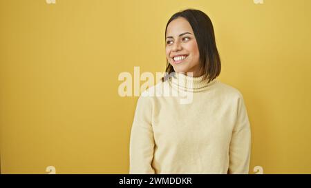 Jeune femme hispanique souriante en pull beige sur un fond jaune vif regardant sur le côté. Banque D'Images