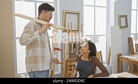 Homme et femme collaborent dans un atelier de menuiserie ensoleillé, entouré d’outils de travail du bois et de cadres en bois. Banque D'Images