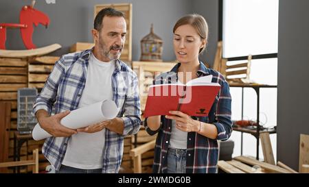 Conversation sérieuse, deux charpentiers professionnels lisant un livre rempli de plans, englouti dans une conversation de menuisier dans un lieu de travail de menuiserie occupé indo Banque D'Images