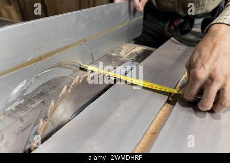 Photo horizontale une vue détaillée des mains d'un menuisier qui mesure les distances sur une lame de scie de table pour une coupe précise, soulignant l'importance Banque D'Images