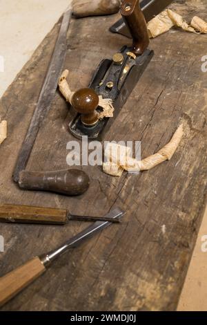 Photo verticale gros plan détaillé d'outils à main de travail du bois, y compris des ciseaux et un rabot à main vintage, sur un établi vieilli avec des copeaux frais. Busi Banque D'Images
