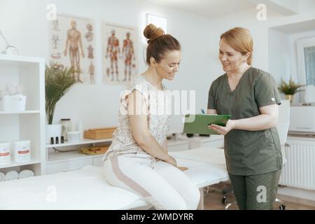 Le temps des soins de santé. thérapeute de massage féminin heureux dans l'armoire de massage avec le client effectuant l'examen et l'écriture dans le presse-papiers. Banque D'Images