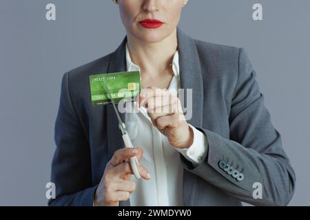 Gros plan sur la femme employée en costume gris avec carte de crédit et ciseaux sur fond gris. Banque D'Images