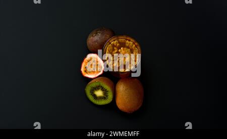 Un verre de jus de fruits avec des graines dans un grand verre sur un fond noir, à côté de morceaux de pitaya et un kiwi mûr. Vue de dessus, pose à plat. Banque D'Images