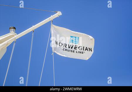 Norwegian Cruise Line logo flag (NCL), le drapeau de la compagnie de croisières basée à Miami vole sur un mât de navire de croisière avec feu de navigation, fond de ciel bleu Banque D'Images