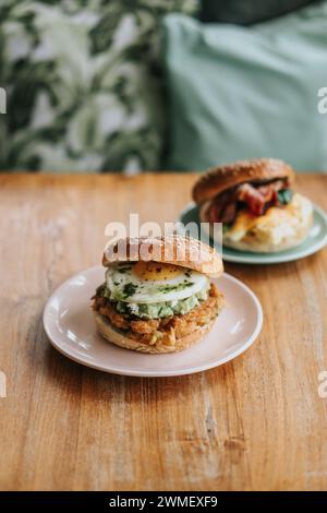 Vue de haut en bas de deux assiettes de sandwichs de petit-déjeuner bagel hamburger, avec œufs, poulet, sauce et végétalien sur une table en bois Banque D'Images