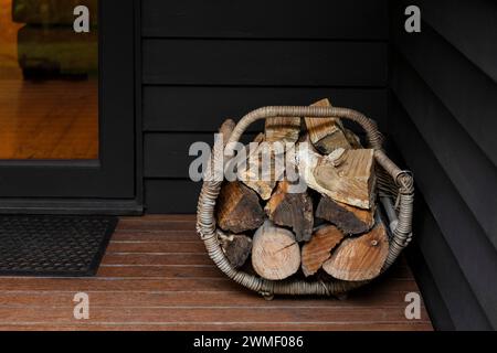 Pile de bois de chauffage dans un panier en osier placé près de l'entrée d'une maison. Banque D'Images