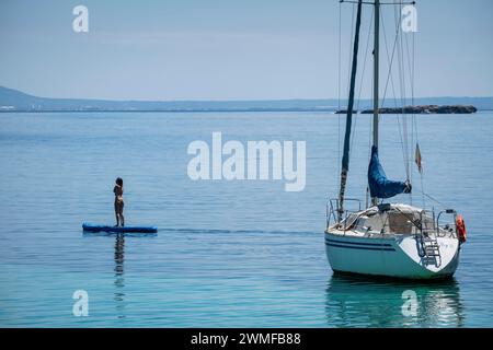 Jeune femme pratiquant le paddle surf à côté d'un voilier, Cala Portals Vells, Calvia, Majorque, Îles Baléares, Espagne Banque D'Images