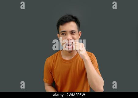 Quelque chose coincé dans les dents d'un jeune homme asiatique, tirant avec une main sur un fond Uni. Banque D'Images