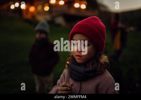 Portrait d'une fille mignonne soufflant une flamme sur un bâton brûlant. La famille ayant un barbecue dans le jardin un soir d'automne. Banque D'Images