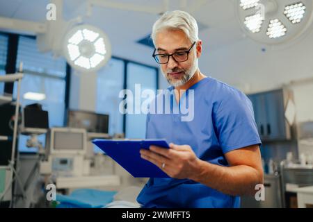 Portrait d'un beau médecin masculin en gommages. ER médecin examinant le patient, lisant le test médical, résultats de laboratoire dans le presse-papiers. ER avec patient vivant Banque D'Images