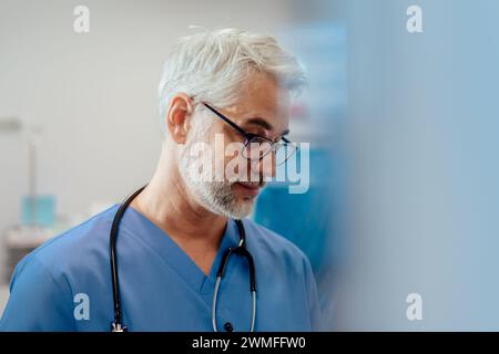 Portrait d'un médecin urgentiste confiant debout aux urgences hospitalières. Beau médecin dans les gommages bleus avec stéthoscope, debout dans les cliniques privées modernes Banque D'Images