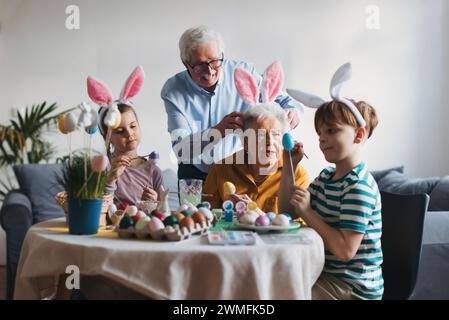 Grand-mère avec de petits enfants décorant des œufs de pâques à la maison. Tradition de peindre les oeufs avec pinceau et colorant d'oeuf de pâques. Banque D'Images