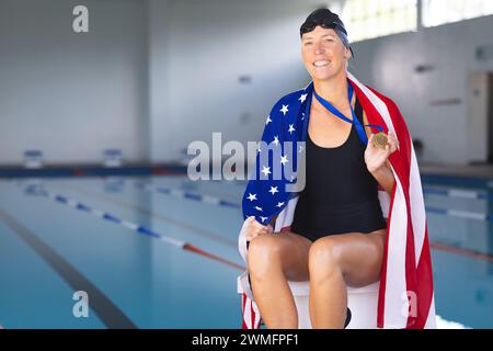 Femme caucasienne célèbre une victoire en natation au bord de la piscine avec le drapeau américain avec une médaille Banque D'Images