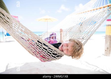 Un garçon heureux qui plonge dans un hamac sur la plage de Shoal Bay à Anguilla Banque D'Images