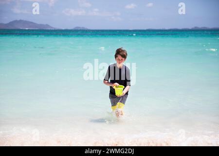 Tween Boy transporte seau marchant hors de la mer des Caraïbes le jour du vent Banque D'Images