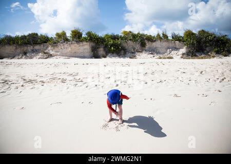 Grand angle de tout-petit garçon dans chapeau seau bleu et ombre sur la plage Banque D'Images
