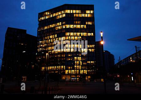 L'immeuble de bureaux illumine la soirée avec des fenêtres qui brillent au crépuscule, mettant en valeur la vie de travail urbaine après les heures de travail Banque D'Images